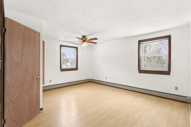 spare room featuring light wood-style floors, a wealth of natural light, a textured ceiling, and baseboard heating