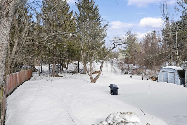 yard layered in snow with a storage shed, an outdoor structure, and fence