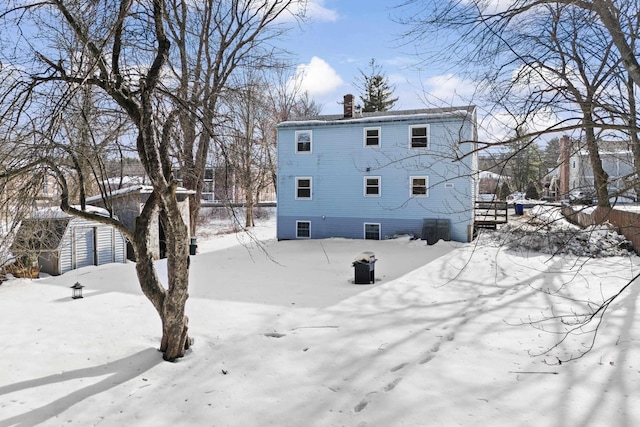 snow covered property featuring an outbuilding, fence, a chimney, and a storage shed