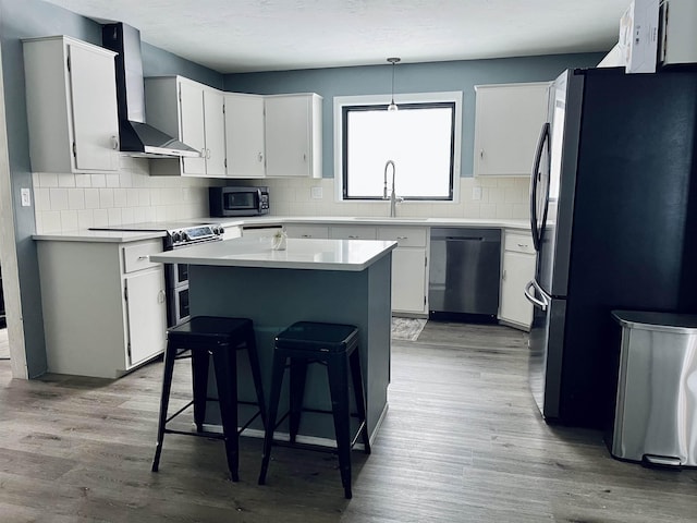 kitchen with wall chimney range hood, appliances with stainless steel finishes, a sink, and wood finished floors