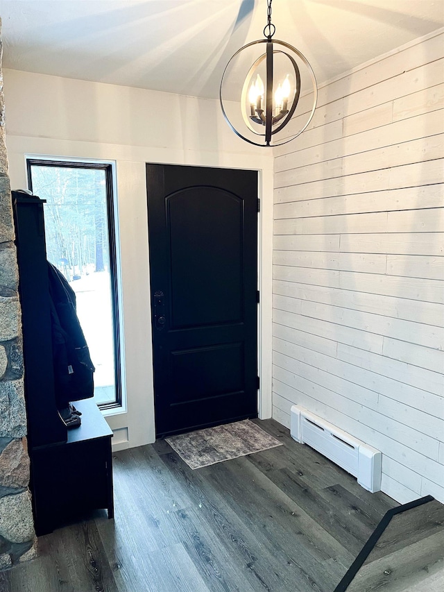 entryway featuring a baseboard heating unit, dark wood finished floors, wood walls, and an inviting chandelier