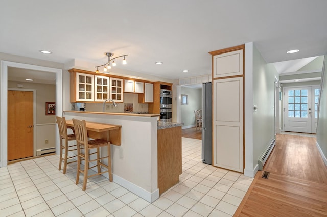 kitchen featuring a baseboard radiator, stainless steel appliances, a peninsula, a sink, and baseboard heating