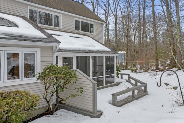 snow covered back of property with a sunroom and a shingled roof