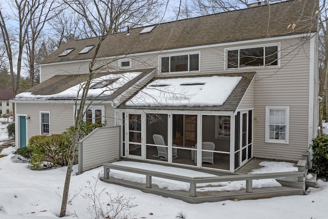 snow covered property featuring a shingled roof and a sunroom