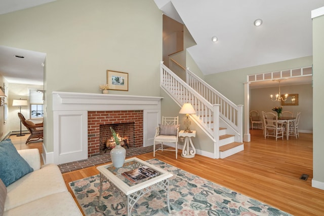 living room with stairway, wood finished floors, an inviting chandelier, a fireplace, and high vaulted ceiling