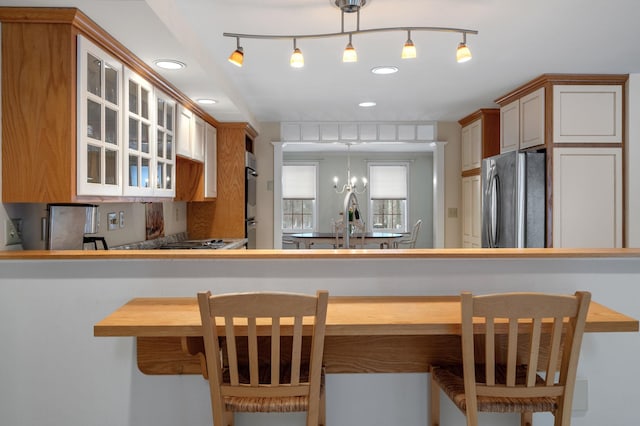 kitchen featuring glass insert cabinets, freestanding refrigerator, a sink, a chandelier, and a kitchen breakfast bar