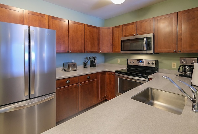 kitchen with light countertops, appliances with stainless steel finishes, brown cabinetry, and a sink