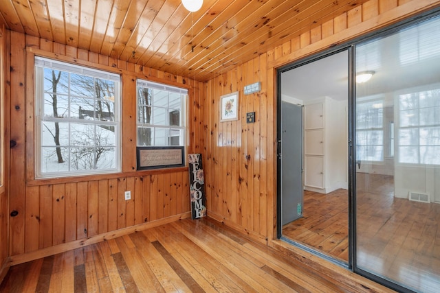 empty room featuring light wood finished floors, a wealth of natural light, wooden ceiling, and visible vents