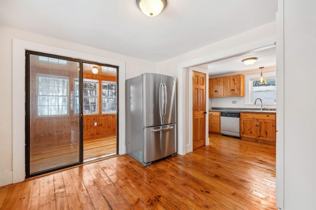 kitchen with a sink, light wood-style floors, freestanding refrigerator, dishwasher, and brown cabinetry