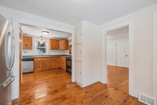 kitchen featuring visible vents, dishwashing machine, black electric range oven, freestanding refrigerator, and a sink