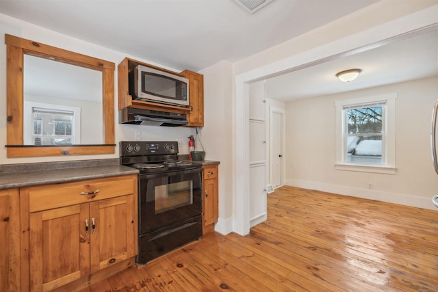 kitchen featuring dark countertops, stainless steel microwave, light wood-type flooring, under cabinet range hood, and black range with electric cooktop