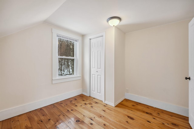 unfurnished bedroom with lofted ceiling, a closet, light wood-style flooring, and baseboards