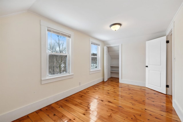 unfurnished bedroom featuring light wood-style floors, a closet, vaulted ceiling, and baseboards