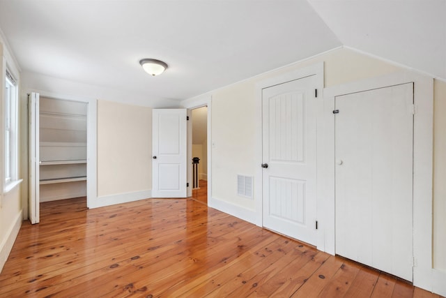 unfurnished bedroom with vaulted ceiling, light wood-type flooring, visible vents, and baseboards