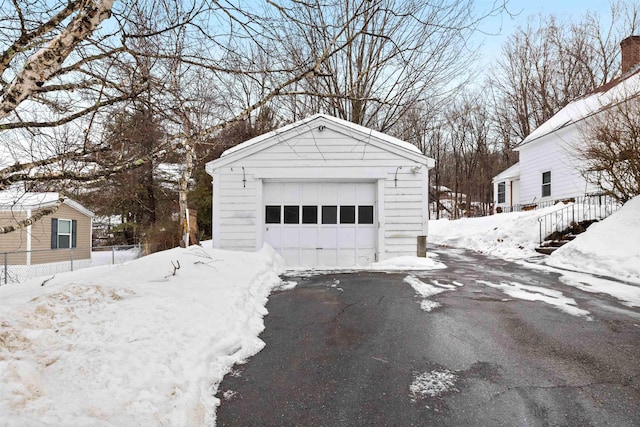 snow covered garage with driveway, a detached garage, and fence