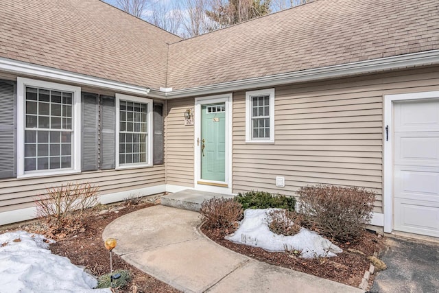 doorway to property with an attached garage and roof with shingles