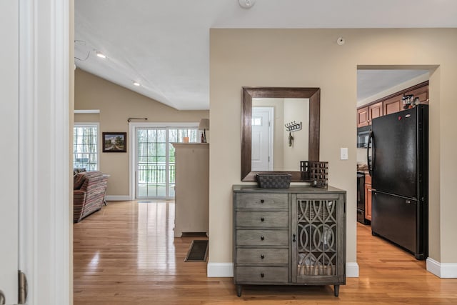 corridor with vaulted ceiling, light wood-style floors, visible vents, and baseboards