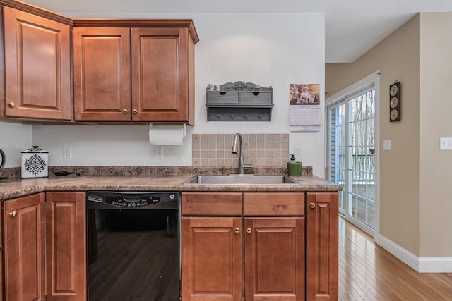 kitchen with brown cabinetry, baseboards, light wood-style flooring, a sink, and black dishwasher