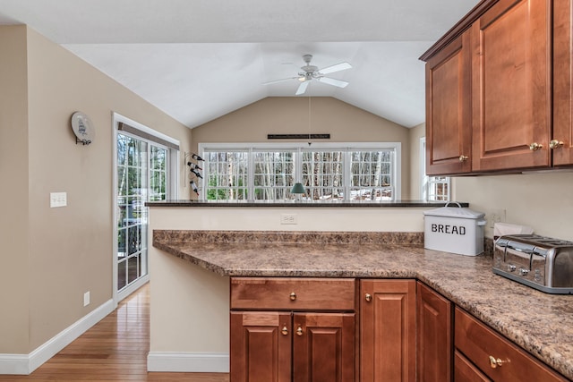 kitchen featuring baseboards, a peninsula, light wood-style flooring, ceiling fan, and vaulted ceiling