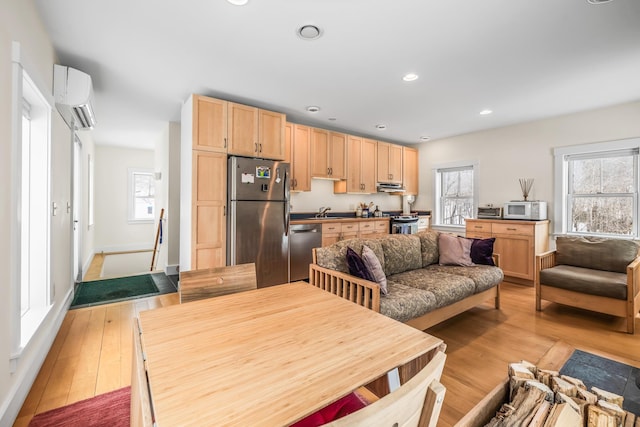 kitchen with light wood-style flooring, stainless steel appliances, an AC wall unit, light brown cabinets, and a wealth of natural light