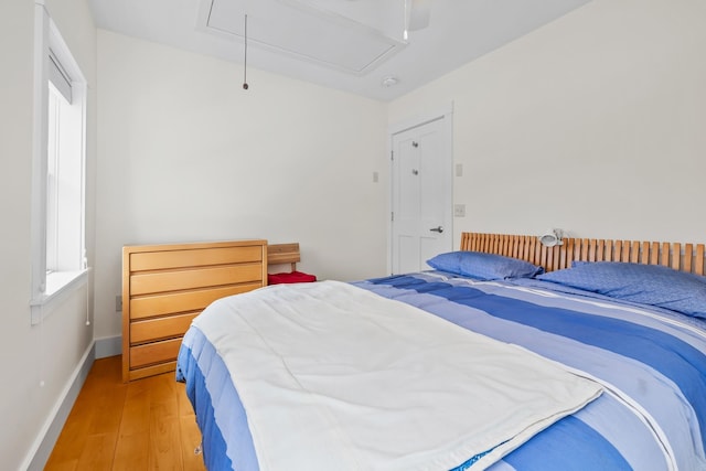 bedroom featuring light wood-type flooring, attic access, and baseboards