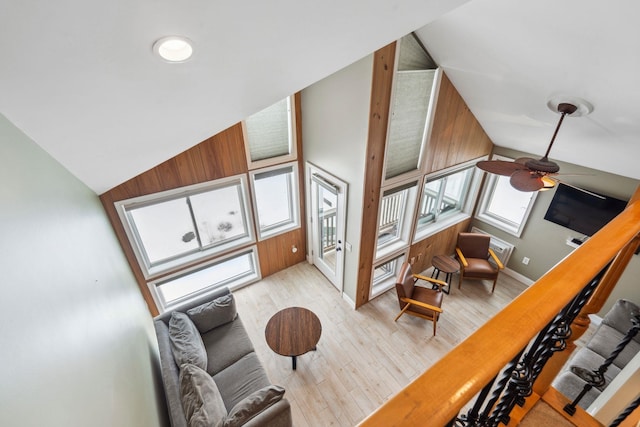 living area with ceiling fan, wood walls, wood finished floors, vaulted ceiling, and stairs