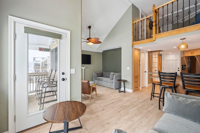 living area featuring ceiling fan, high vaulted ceiling, baseboards, stairway, and light wood-type flooring