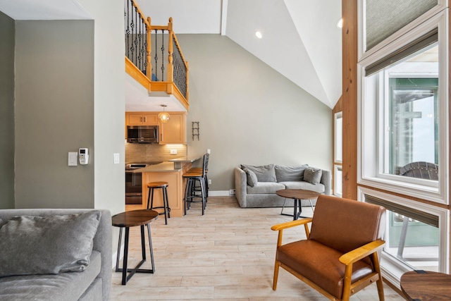 living area featuring high vaulted ceiling, recessed lighting, light wood-style flooring, and baseboards