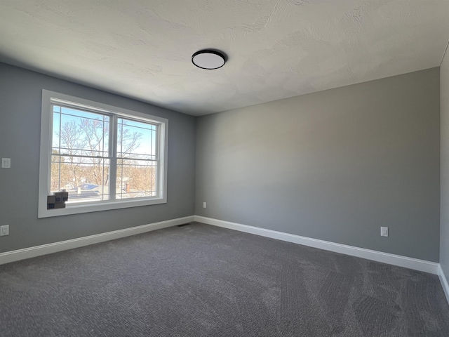 empty room featuring baseboards, dark carpet, and a textured ceiling