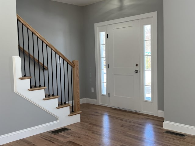 foyer entrance featuring visible vents, stairway, baseboards, and wood finished floors