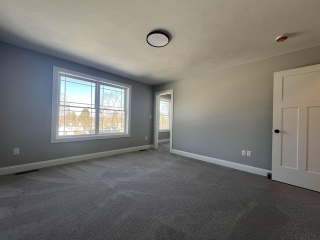 spare room featuring dark carpet, visible vents, and baseboards