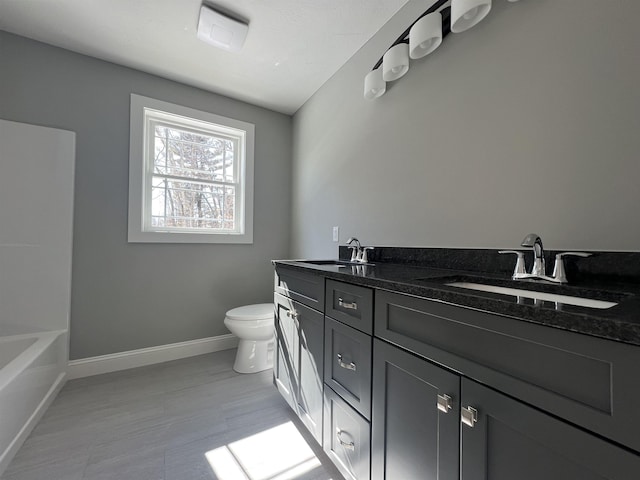 full bathroom featuring double vanity, baseboards, toilet, a bathtub, and a sink