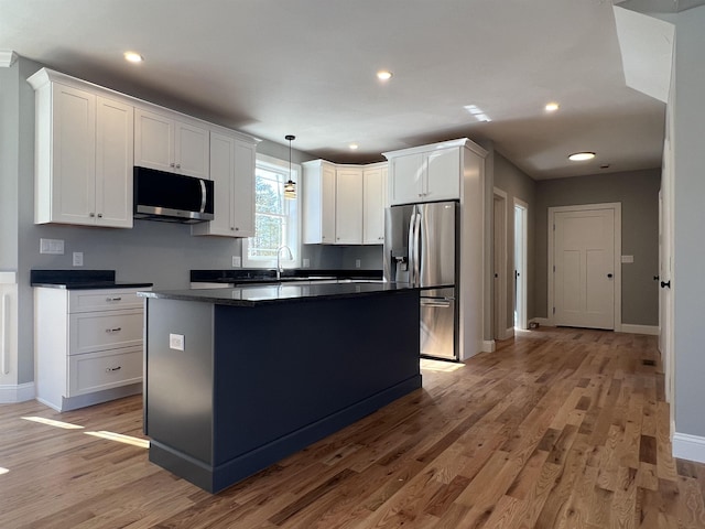 kitchen with light wood finished floors, white cabinets, dark countertops, a kitchen island, and stainless steel appliances