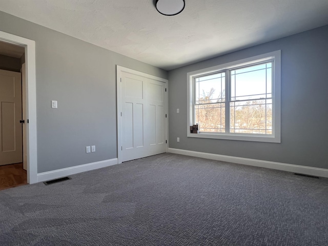 unfurnished bedroom with a closet, carpet flooring, visible vents, and baseboards