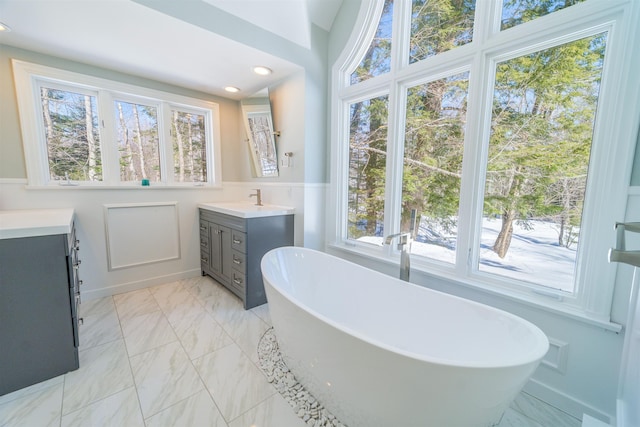 bathroom with marble finish floor, a healthy amount of sunlight, a soaking tub, and vanity