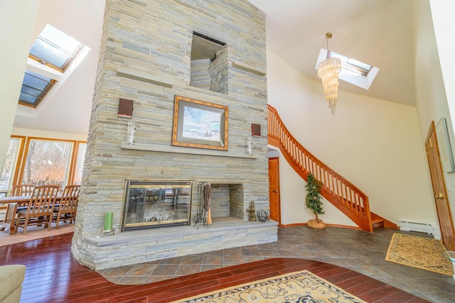 unfurnished living room with a skylight, a baseboard radiator, a stone fireplace, wood finished floors, and high vaulted ceiling