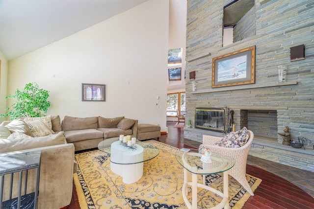 living area featuring high vaulted ceiling, a stone fireplace, and wood finished floors