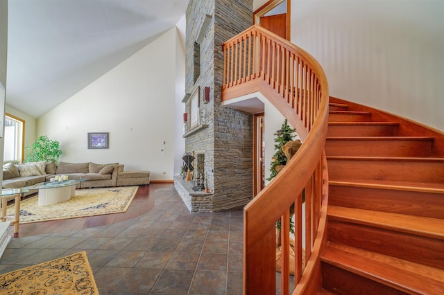 staircase with high vaulted ceiling and a stone fireplace