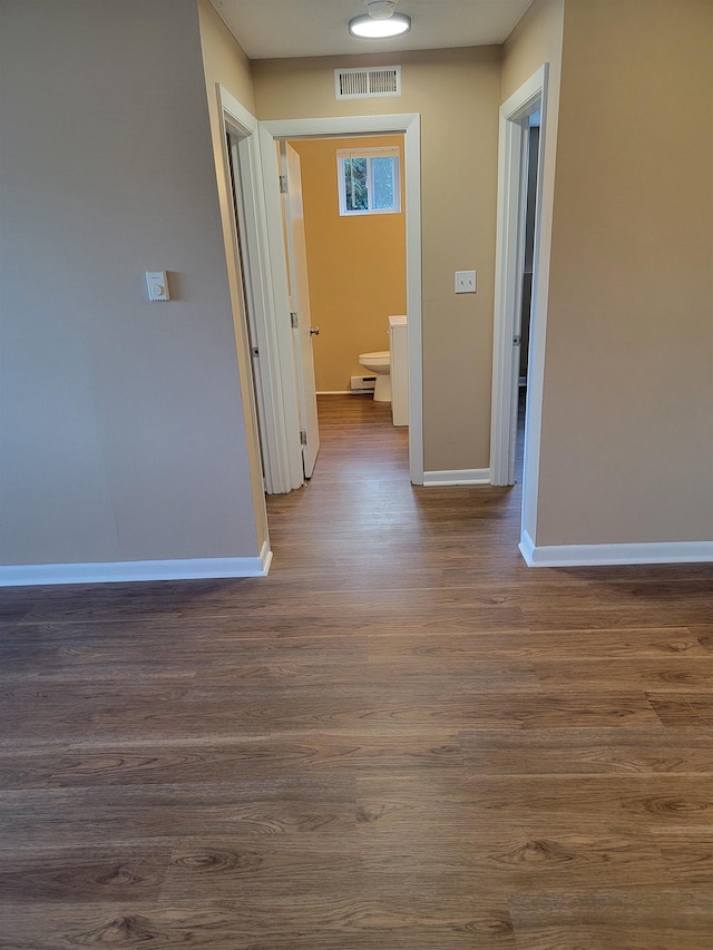 corridor featuring a baseboard heating unit, visible vents, dark wood finished floors, and baseboards