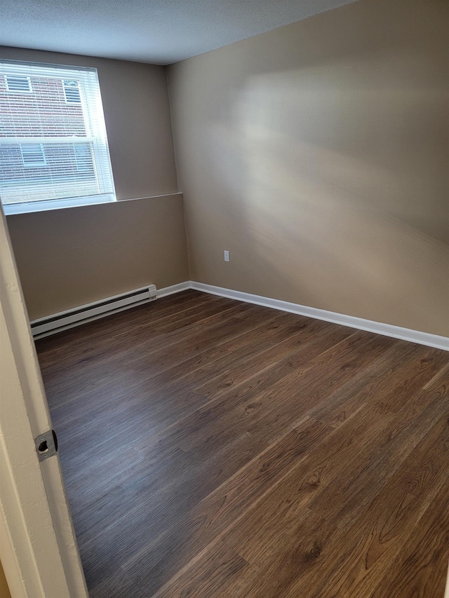 spare room featuring dark wood-style floors, baseboard heating, and baseboards