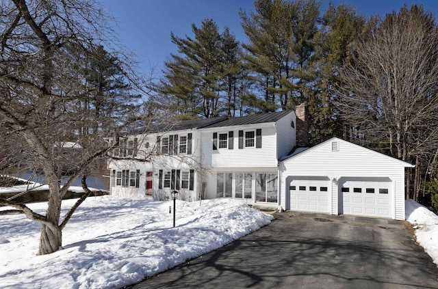 view of front facade with driveway, a chimney, metal roof, an attached garage, and a standing seam roof