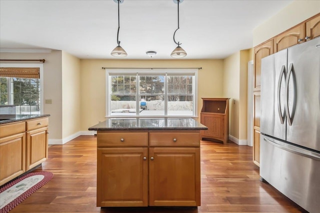 kitchen featuring freestanding refrigerator, hanging light fixtures, dark stone countertops, and wood finished floors