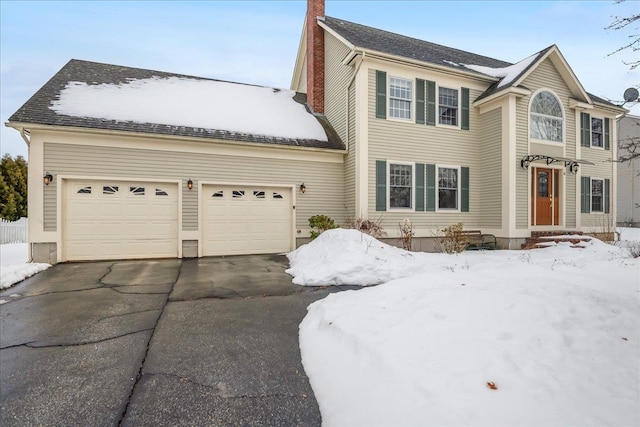 view of front facade with an attached garage, a chimney, and aphalt driveway