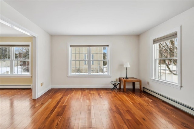 spare room featuring baseboard heating, wood-type flooring, and baseboards