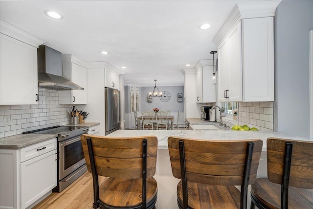 kitchen with a sink, white cabinetry, wall chimney range hood, appliances with stainless steel finishes, and light stone countertops