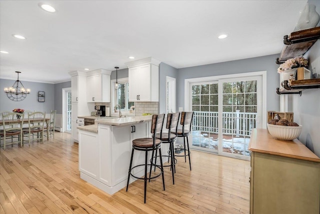 kitchen featuring a peninsula, tasteful backsplash, light wood-style flooring, and white cabinetry