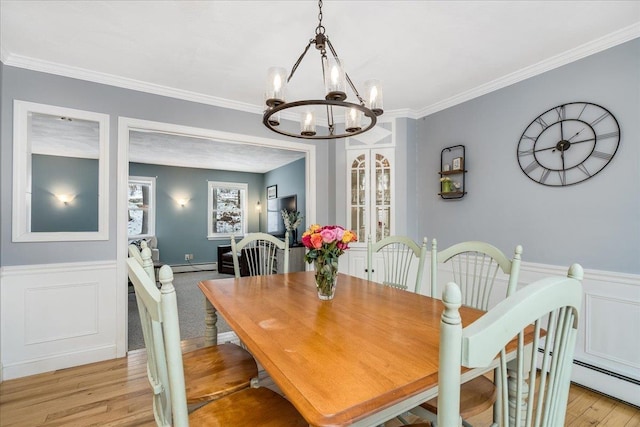 dining area with a notable chandelier, a baseboard heating unit, a wainscoted wall, light wood-type flooring, and crown molding