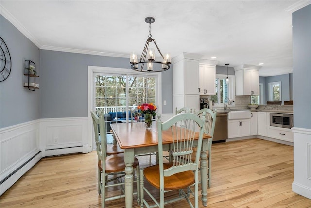 dining space with a notable chandelier, wainscoting, light wood-style flooring, and crown molding