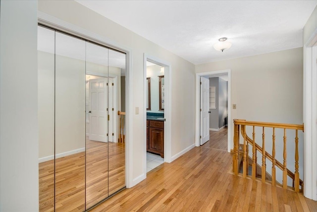 hall featuring baseboards, light wood finished floors, and an upstairs landing