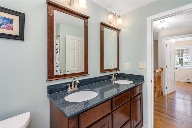 full bath featuring double vanity, a sink, toilet, and wood finished floors